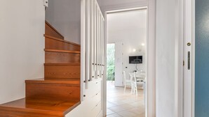 Een houten trap met witte leuningen, leidend naar een kamer met een betegelde vloer en een aan de muur bevestigde televisie.