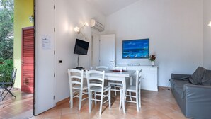Een compacte woonruimte met een eethoek, een bank, een televisie en een schilderij aan de muur.