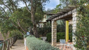 Een pad van stenen leidt naar een landelijk gebouw met een houten pergola en een bank.