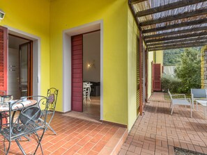 A bright yellow exterior wall with a tiled patio area, a metal chair, and a table with a coffee pot.