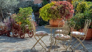 Eine Terrasse mit Steinboden, Metallstühlen und -tischen, umgeben von Topfpflanzen und einer Steinmauer.