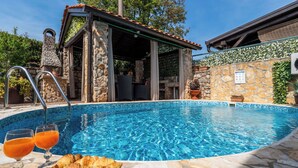 Une piscine aux bords recouverts de pierres, un espace détente abrité et une assiette de croissants.