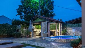 Un jardin avec un barbecue en pierre, une piscine et des chaises longues.