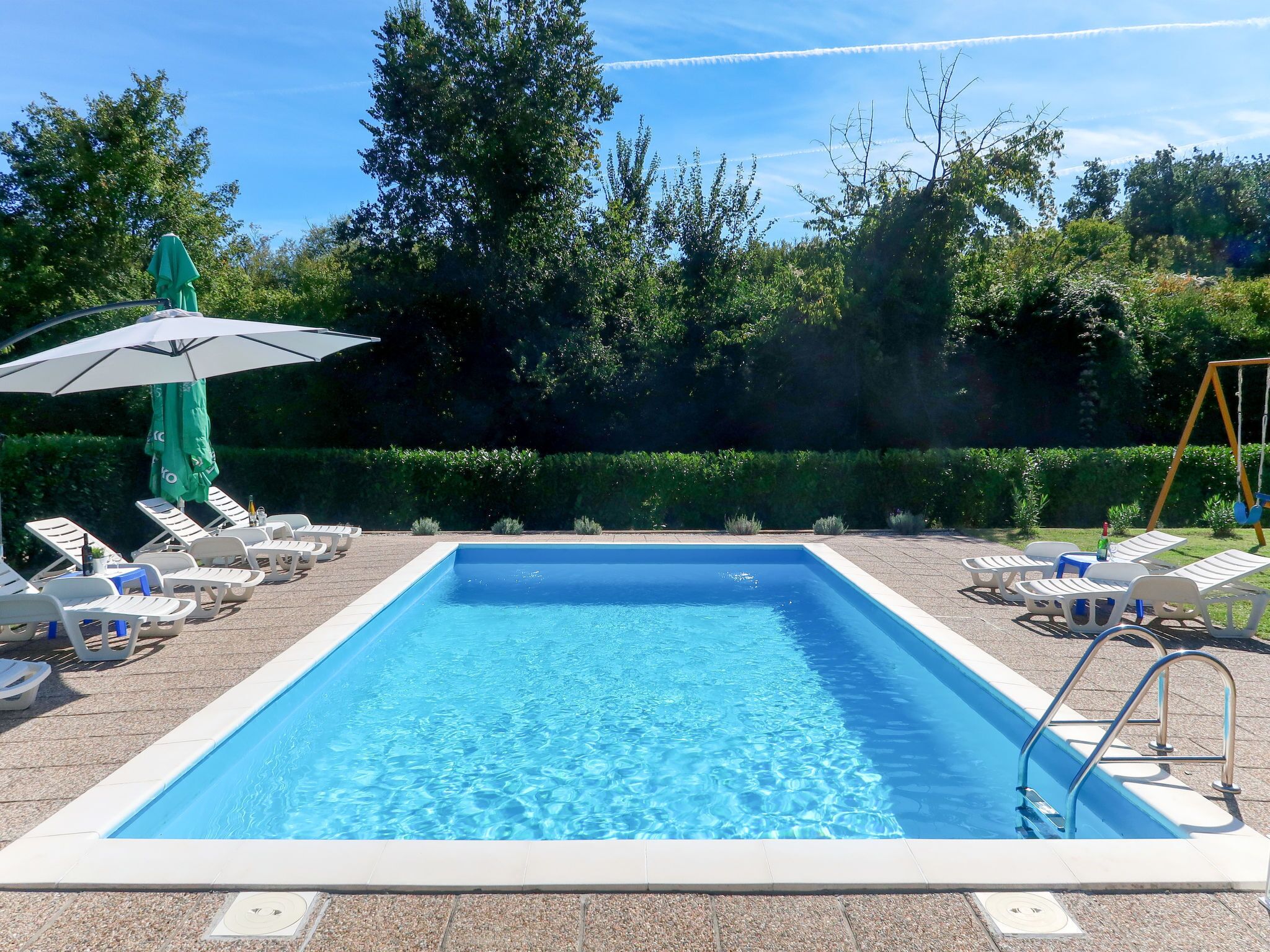 Una piscina rectangular con agua azul cristalina, rodeada de sillas de descanso y sombrillas.