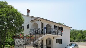 A two-story building with a balcony, a staircase, and a car parked in front.