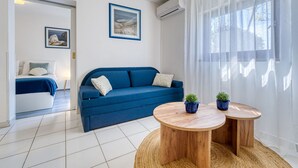 Ein modernes Wohnzimmer mit einem blauen Sofa, zwei Holznachttischen und einem großen Fenster mit transparenten Vorhängen.
