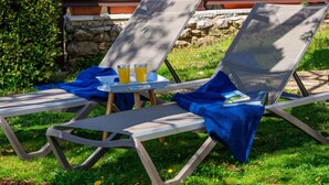 Zwei Lounge-Stühle mit Tablett und Getränken vor einer Steinwand und Grünpflanzen.