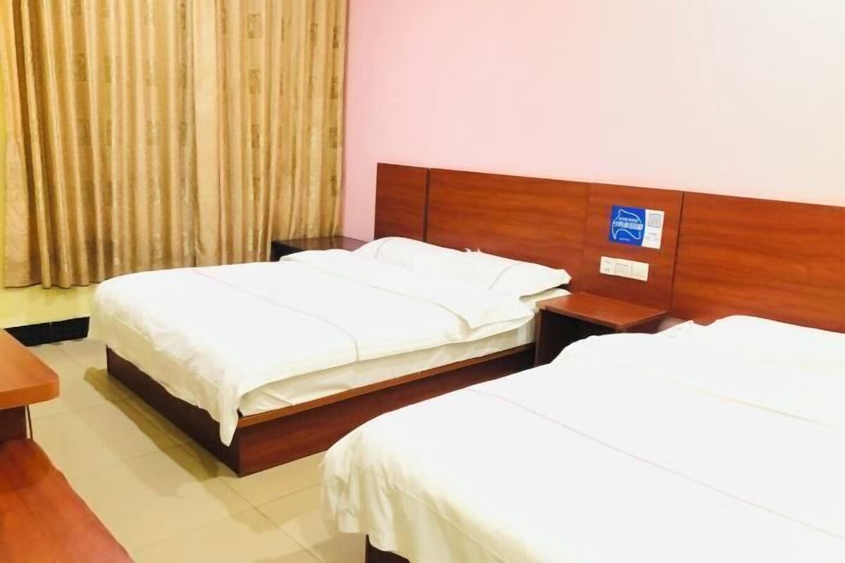 A hotel room with two single beds, wooden headboards, a nightstand, and a curtain.