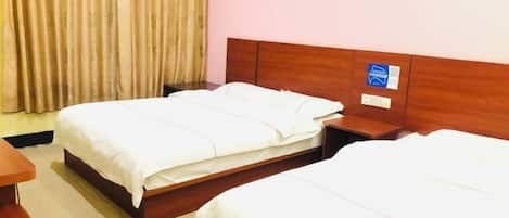 A hotel room with two single beds, wooden headboards, a nightstand, and a curtain.
