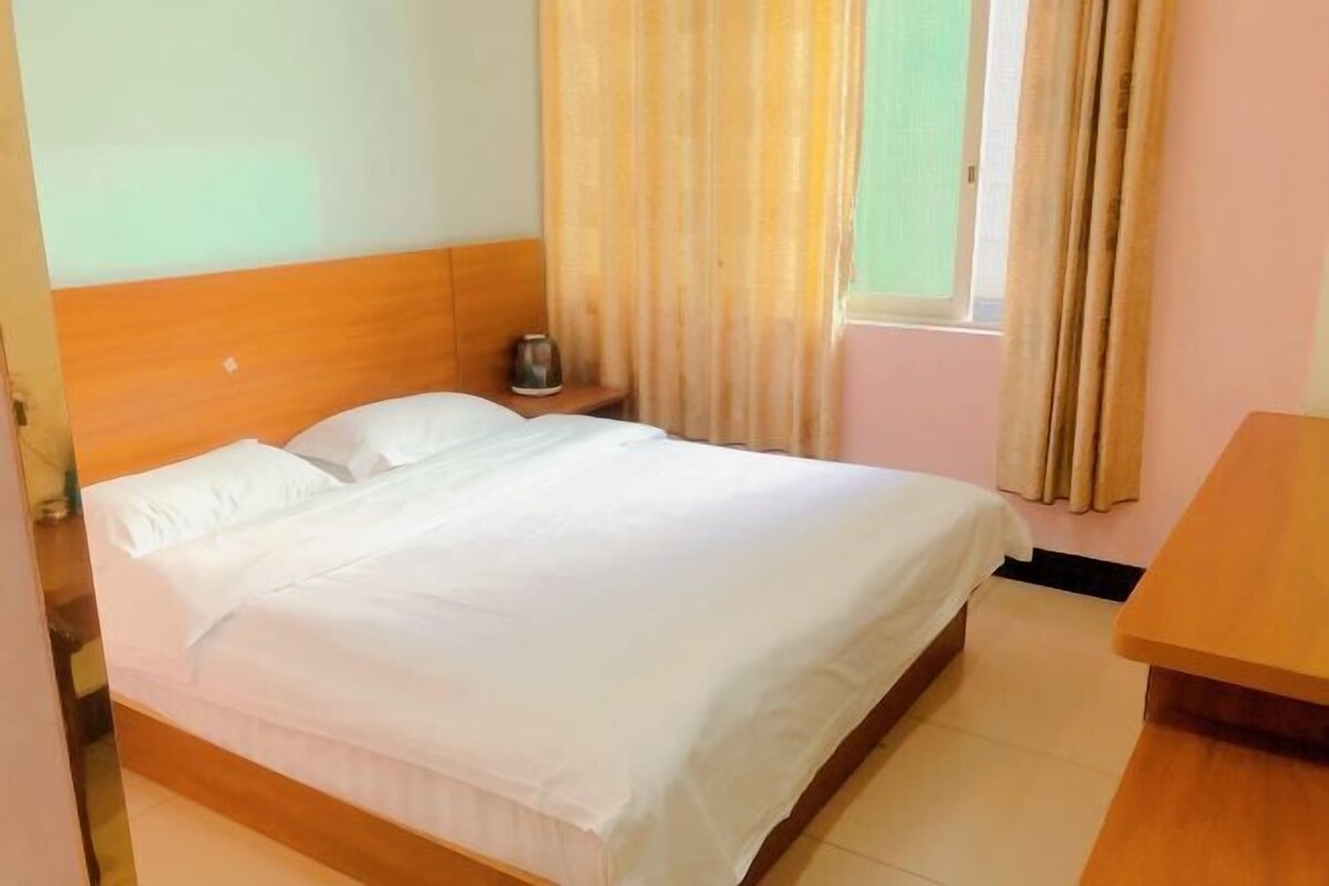 A hotel room with a bed, a nightstand, a window with curtains, and a wooden table.