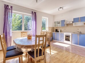 Una cocina moderna con armarios azules, una mesa redonda con sillas y ventanas grandes con cortinas moradas.