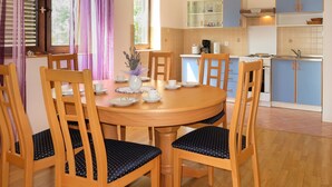 A dining area with a round wooden table surrounded by six wooden chairs with dark patterned cushions. A vase with flowers is placed on the table. - Katarina by Interhome (Lovran)