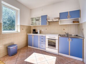 A compact kitchen with blue cabinets, a built-in oven, and a window overlooking greenery. - Katarina by Interhome (Lovran)
