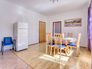 A room with a dining table, chairs, a refrigerator, and a blue plastic chair.