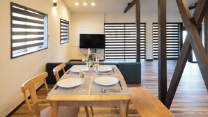 Un coin repas avec une table en bois dressée pour quatre personnes, un canapé et un téléviseur fixé au mur.