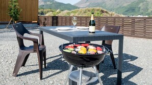 Un espace extérieur aménagé pour les repas, avec un barbecue, une table, des chaises et une bouteille de champagne.