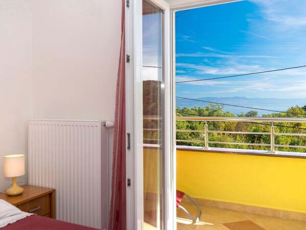 A bedroom with a view of a balcony, a radiator, a bedside table with a lamp, and a window with curtains. - Apartment Andrea by Interhome (Mošćenička Draga)