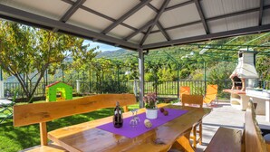 Eine Terrasse im Freien mit einem Holztisch, Bänken und einem Backofen aus Ziegeln.