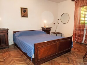 Une chambre à coucher avec un lit en bois, une table de chevet, une petite table avec une lampe, un miroir fixé au mur et un cadre photo.