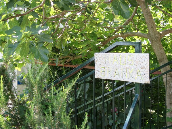 Une enseigne indiquant « HAUTE FRANKA » est fixée à un portail en métal, le tout étant entouré d’une végétation luxuriante.