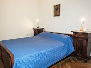 Un dormitorio con una cama, mesitas de noche de madera, una lámpara de pared e imagen enmarco.