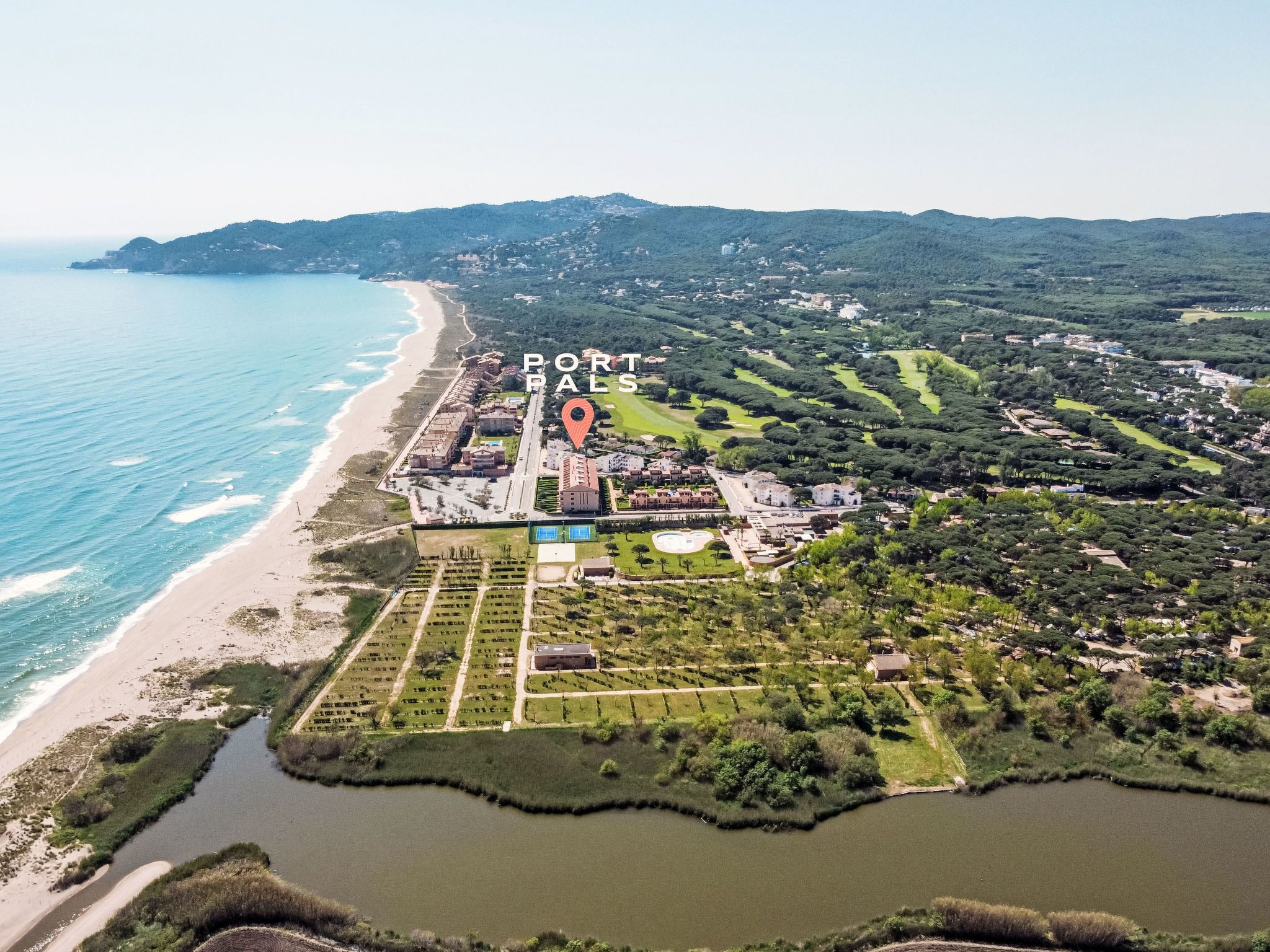 An aerial view of Portals, featuring a beachfront, a golf course, and a large building complex.