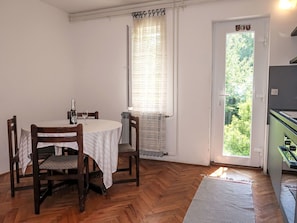 Un coin repas avec une table ronde, des chaises en bois, une fenêtre avec des rideaux et une porte donnant sur l’extérieur.