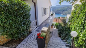 A stone pathway leading to a white building with a balcony overlooking a scenic coastal view. - Katarina by Interhome (Rabac)