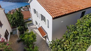 A white building with a red-tiled roof, a balcony, and a view of a body of water and hills. - Katarina by Interhome (Rabac)