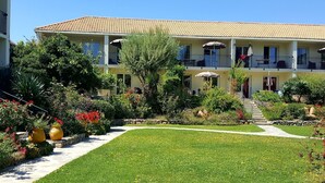 A two-story building with a tiled roof, a garden with various plants and flowers, and a pathway leading to the entrance. - petite maison, 28-30 m², 2 pers by Interhome (Calvi)