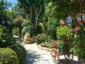 Stroll along the serene garden pathway to a charming cart, surrounded by lush greenery and flowering plants.