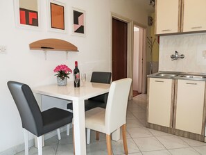 Zona pranzo con tavolo bianco, sedie bianche e nere, una bottiglia di vino e un vaso con fiori rosa.