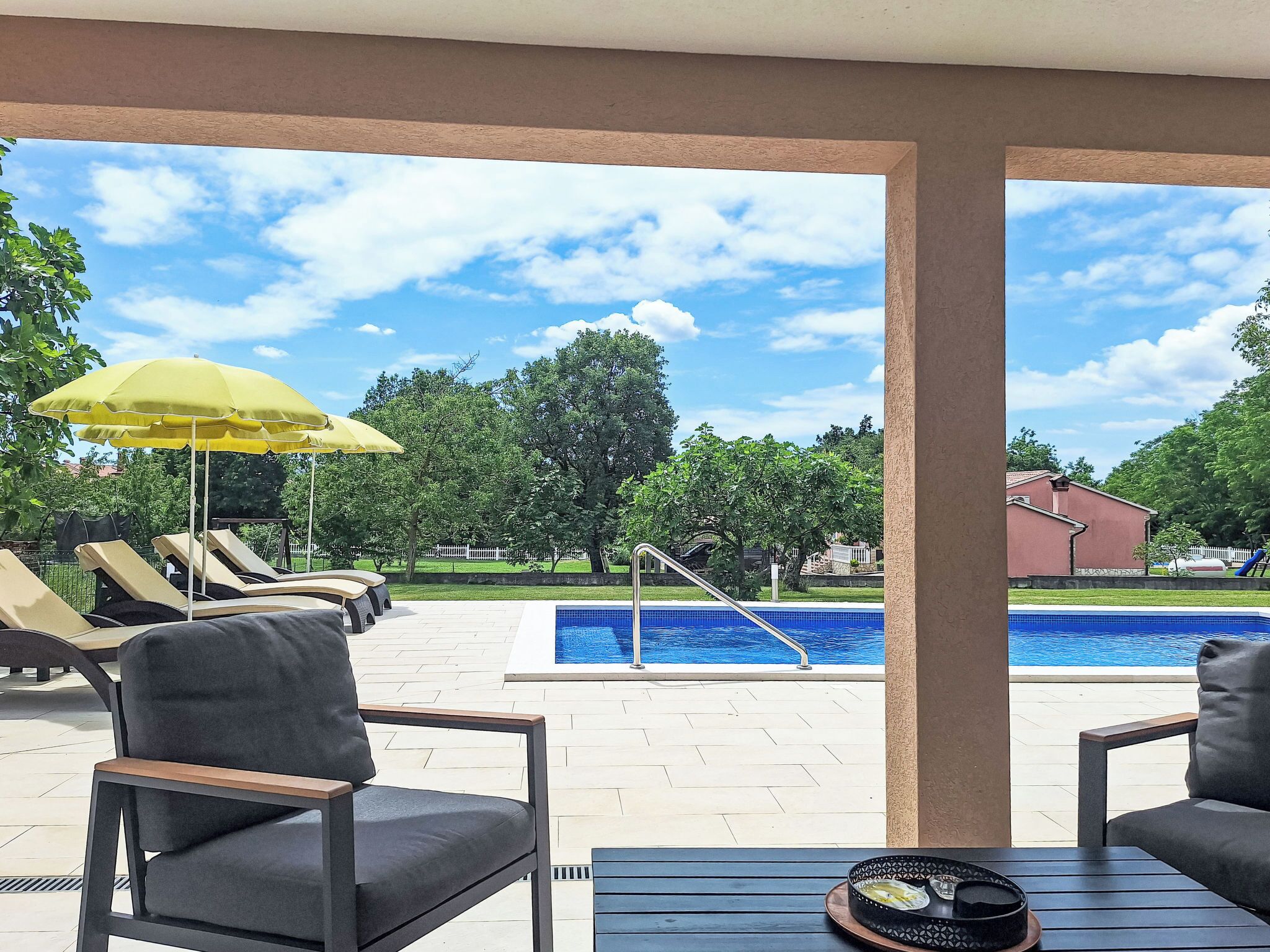 A poolside area with lounge chairs, a yellow umbrella, and a view of a swimming pool.