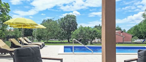 A poolside area with lounge chairs, a yellow umbrella, and a view of a swimming pool.