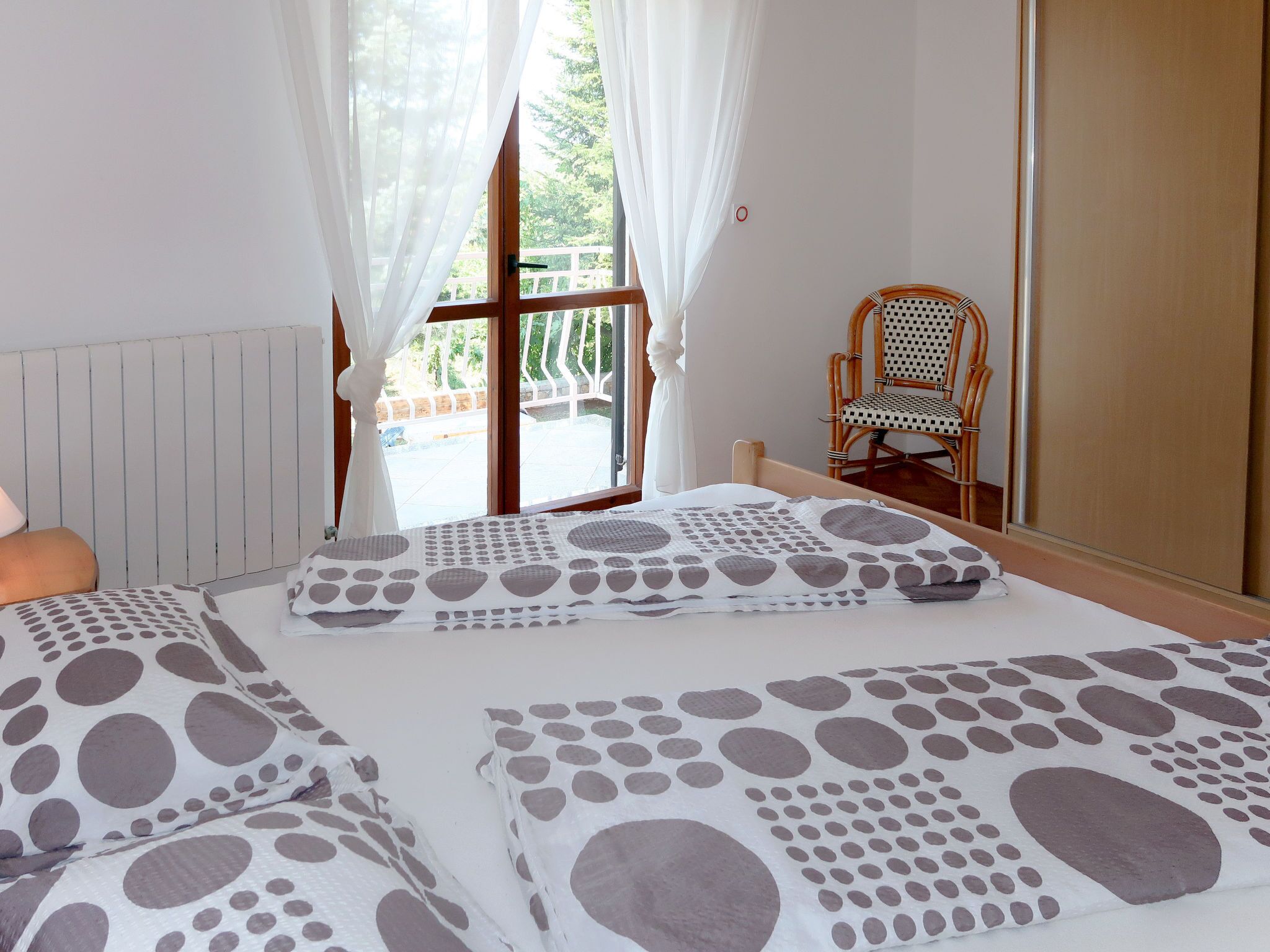 A bedroom with two beds, a wooden chair, and a window with curtains.