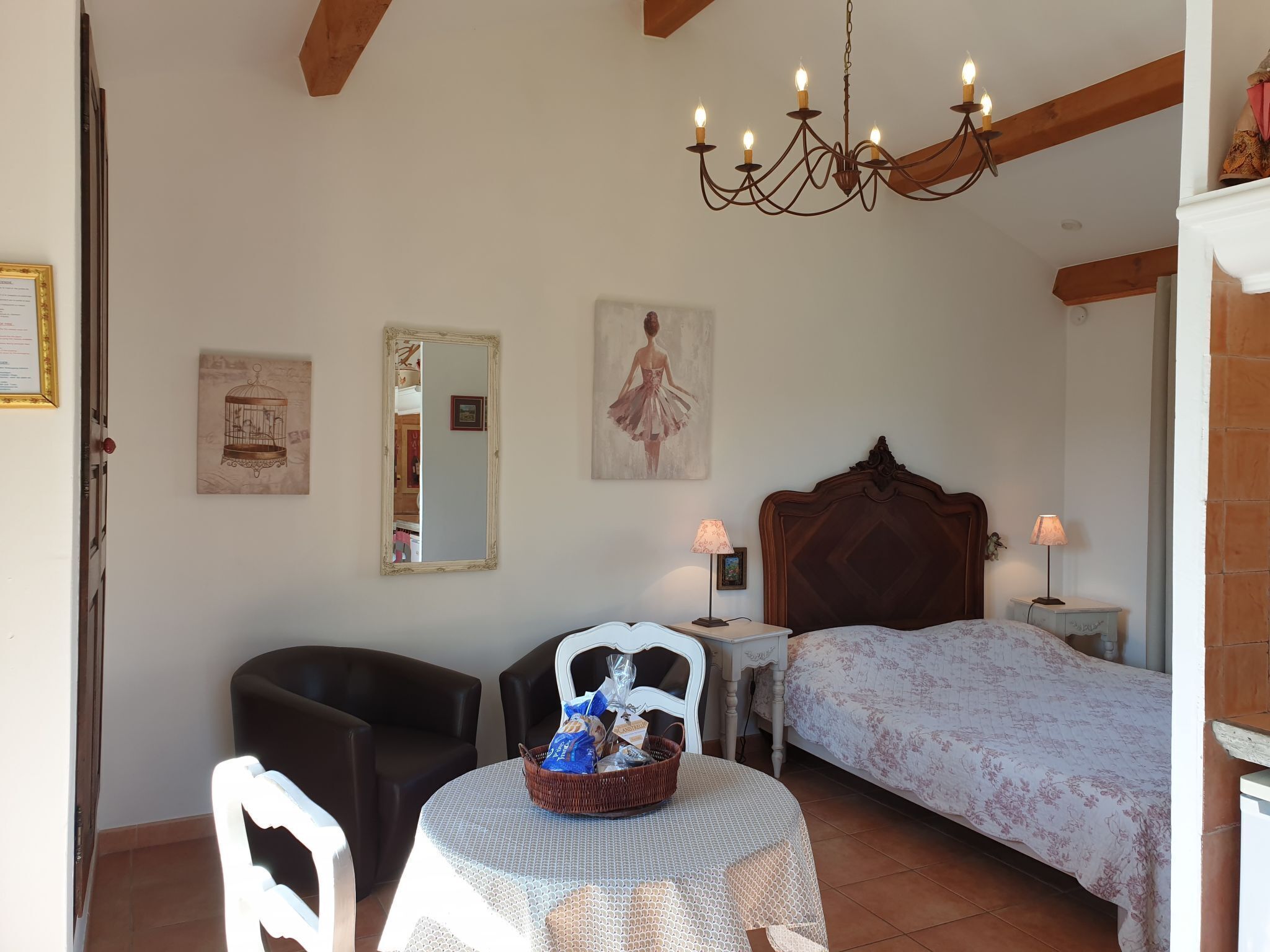 Une chambre à coucher comprenant un lit, une chaise, une table avec un panier, un lustre et un miroir.