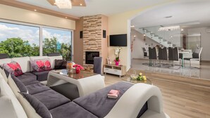 A modern living room with a large sofa, a fireplace, a dining area with a glass table, and a staircase leading to an upper level. - Villa Gabriel by Interhome (Labin)