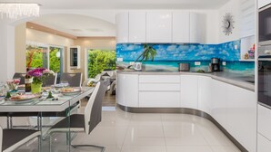A modern kitchen with white cabinets, a curved island, and a tropical beach mural backsplash. - Villa Gabriel by Interhome (Labin)