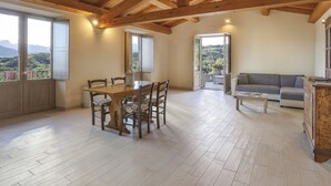 Een ruime woonkamer met een houten plafond, een eettafel met stoelen, een bank en uitzicht op de bergen door grote ramen.