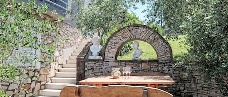 A stone staircase leading to a wooden bench and table set against a stone wall, with a bust sculpture above.