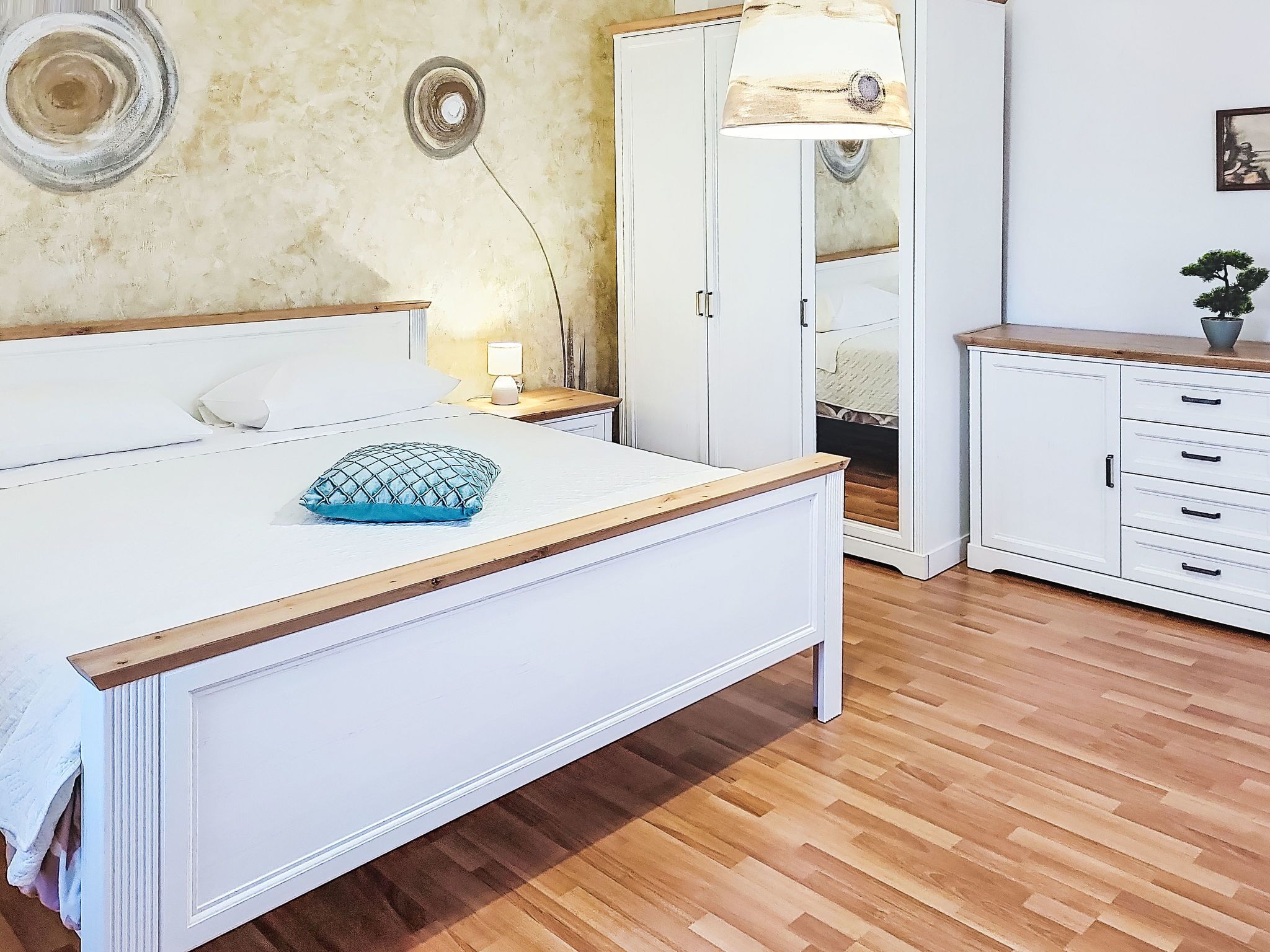 A bedroom with a bed, bedside table, lamp, wardrobe, and a small cabinet.