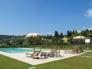 A pool area with lounge chairs and umbrellas, surrounded by greenery and hills. - Melissa by Interhome (Lucca)