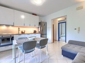 A modern kitchen with white cabinets, a stainless steel refrigerator, and a dining area with a table and chairs.