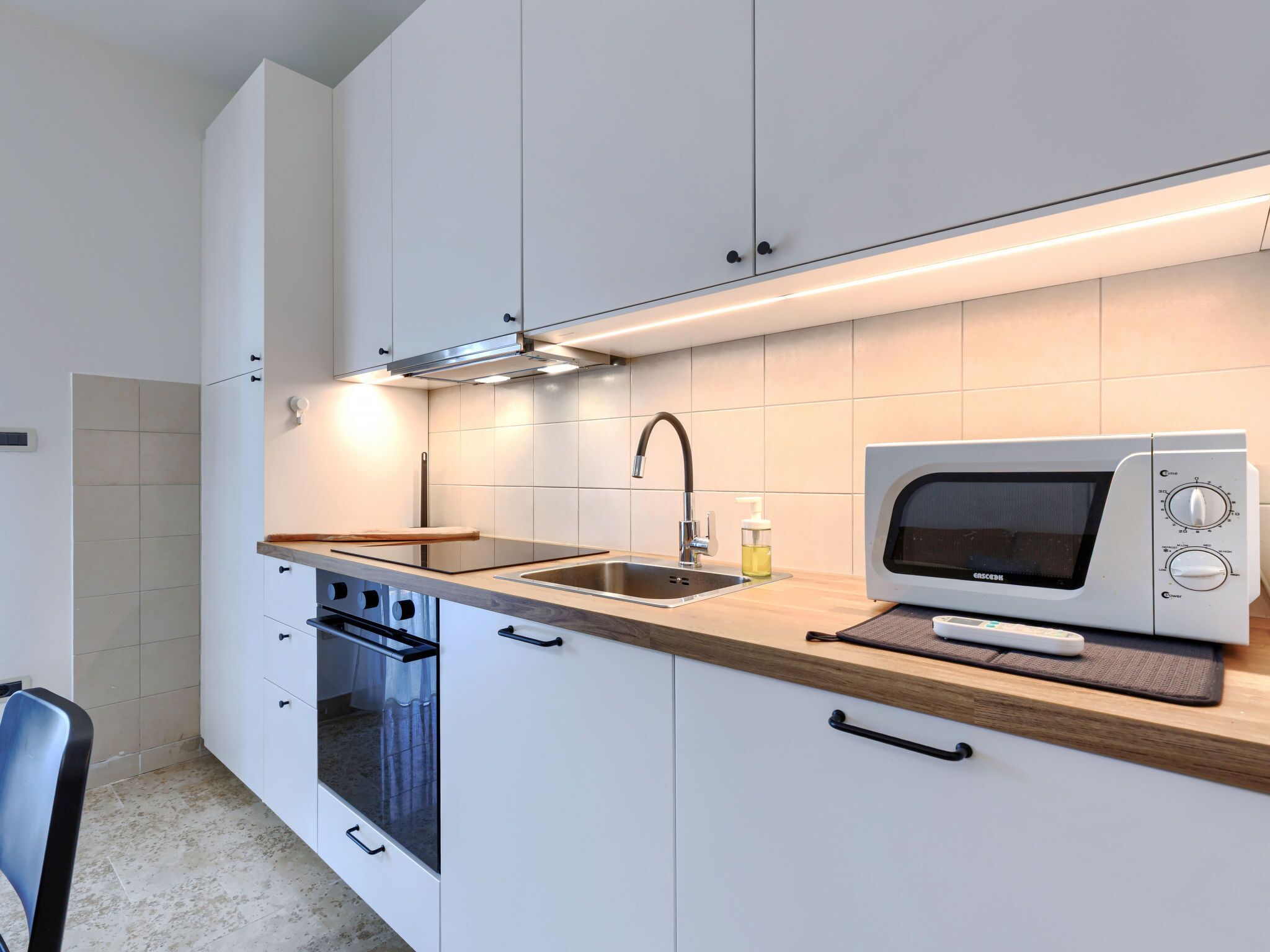 A modern kitchen with white cabinets, a stainless steel sink, a microwave, and a built-in oven.