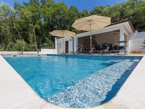 Una piscina amb gandules i ombrel·les, envoltada d'arbres.