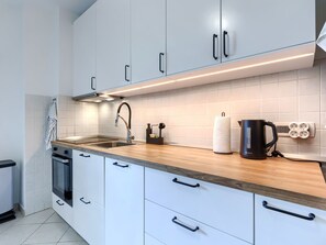A modern kitchen with white cabinets, a wooden countertop, a stainless steel sink, and a coffee maker.