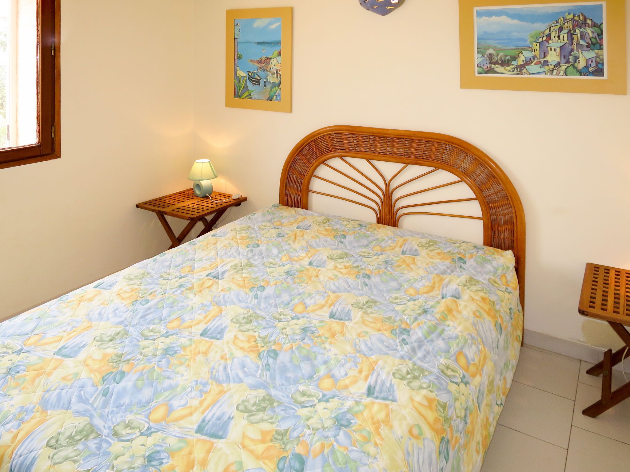 Una camera da letto con un letto, un comodino, una lampada e due quadri appesi al muro.