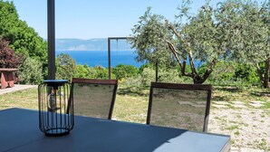 Une table et des chaises d’extérieur, un luminaire suspendu et une vue sur la mer et les arbres.