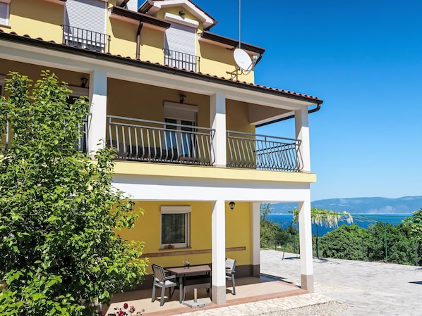 Un edificio de dos pisos con balcones, un patio con mesa y sillas, y vista al mar.