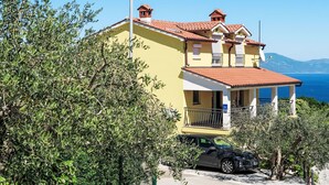 Un immeuble de deux étages, avec un toit recouvert de tuiles rouges, un balcon et une vue sur la mer.